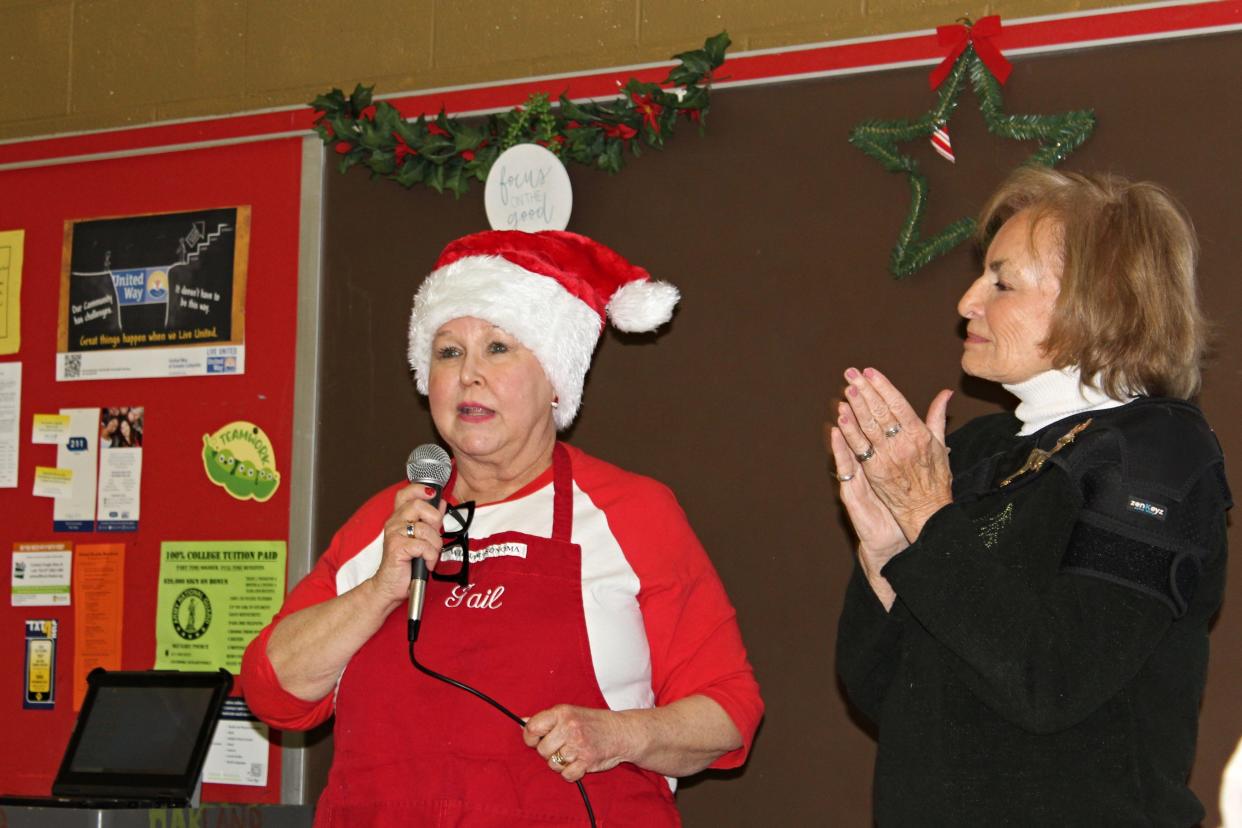 Gail McCormick (left) and Faye Cole (right) speak to Oakland Academy students about the fight against cancer during a holiday celebration Thursday, Dec. 21, 2023. Cole accepted a $300 donation on behalf of the Community Cancer Network from money raised by a student bake sale.