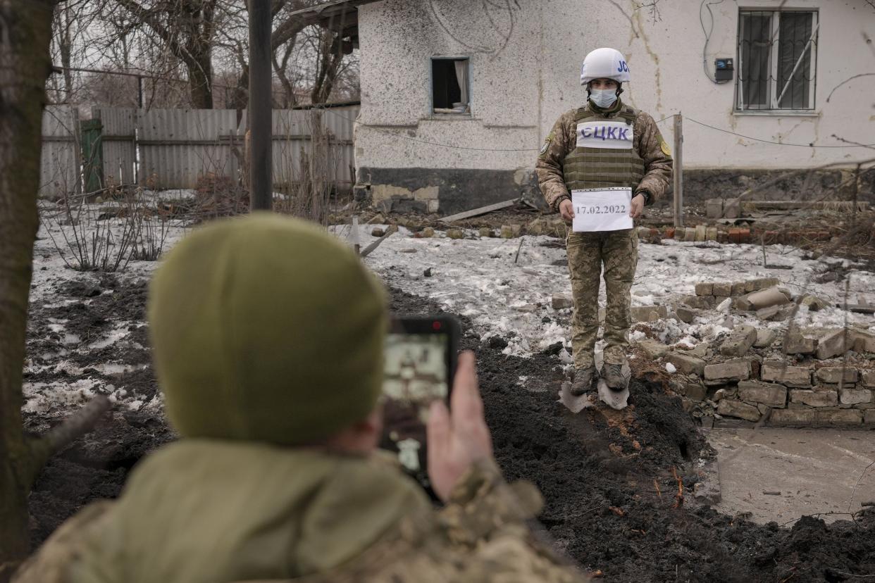 Members of the Joint Centre for Control and Coordination on ceasefire of the demarcation line, or JCCC, take forensic photos of a crater and damage to a house from an artillery shell that landed in Vrubivka, one of the at least eight that hit the village today, according to local officials, in the Luhansk region, eastern Ukraine, Thursday, Feb. 17, 2022.