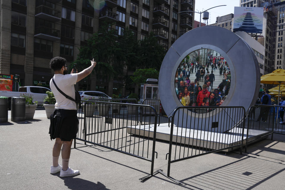 A man signals to pedestrians in Dublin, Ireland through a livestream portal as part of an art installation on the street in New York, Tuesday, May 14, 2024. (AP Photo/Seth Wenig)
