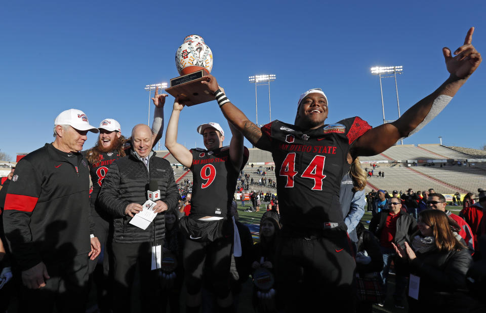 San Diego State linebacker Kyahva Tezino (44), quarterback Ryan Agnew (9), tight end Parker Houston, second from left, and coach Rocky Long, left, celebrate with the trophy after their team beat Central Michigan in the New Mexico Bowl NCAA college football game on Saturday, Dec. 21, 2019 in Albuquerque, N.M. (AP Photo/Andres Leighton)