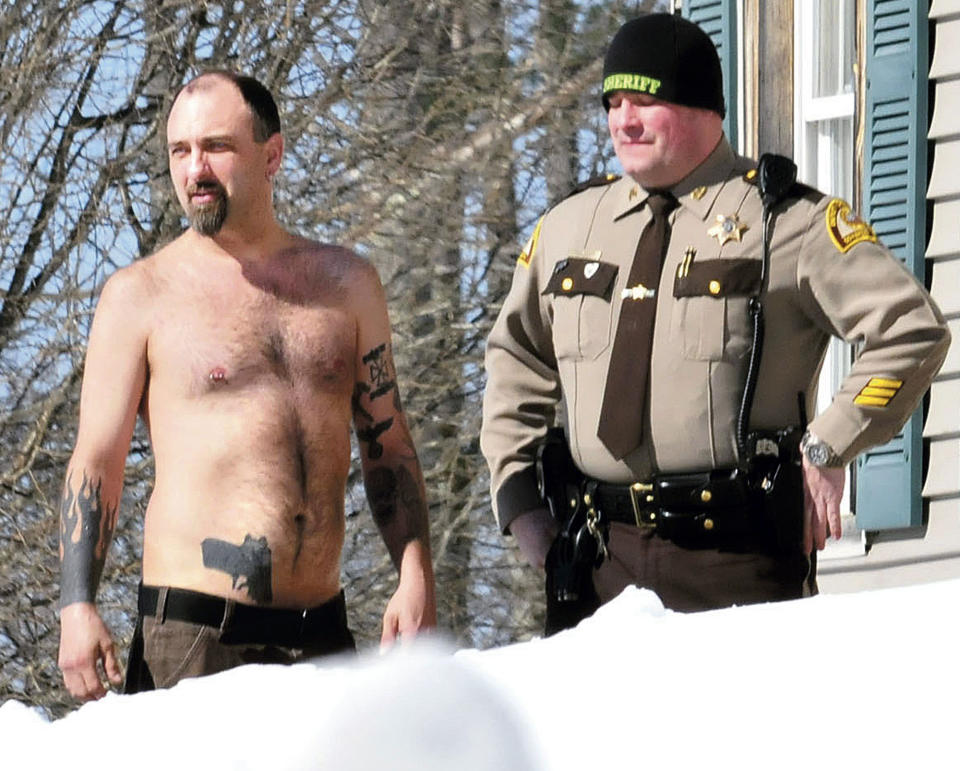 In this Tuesday, March 18, 2014 photo, Michael Smith, left, stands beside a Somerset County Sheriff deputy outside his home in Norridgewock, Maine. Officers armed with assault rifles descended on Smith's home after members of a tree removal crew he'd told to clear off his property reported that he had a gun. The "gun" the tree crew had seen on Smith actually was a life-sized tattoo of a handgun on his stomach. (AP Photo/Morning Sentinel, David Leaming)