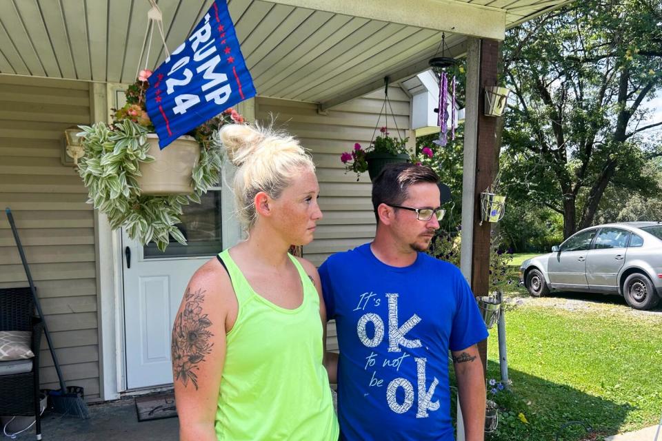 Jessica Lynch and fiance Robert Runyan stand in front of a house with a Trump 2024 flag hanging above the porch.