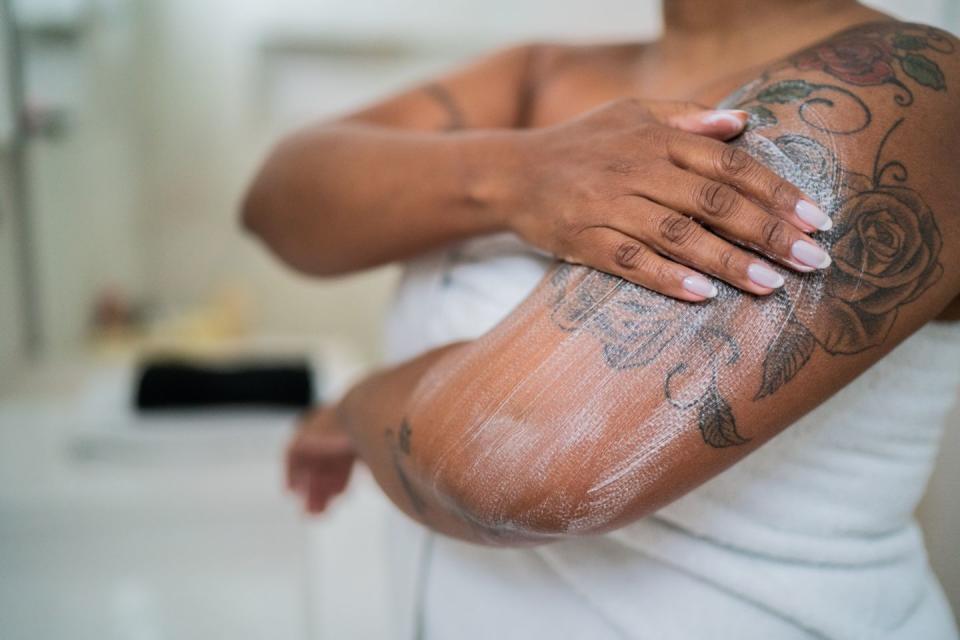 woman applying body lotion over tattoo on arm in the bathroom at home