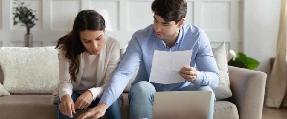 Payday. Concentrated attentive millennial spouses sitting on couch at home discussing possibility of taking out a refinance mortgage loan.