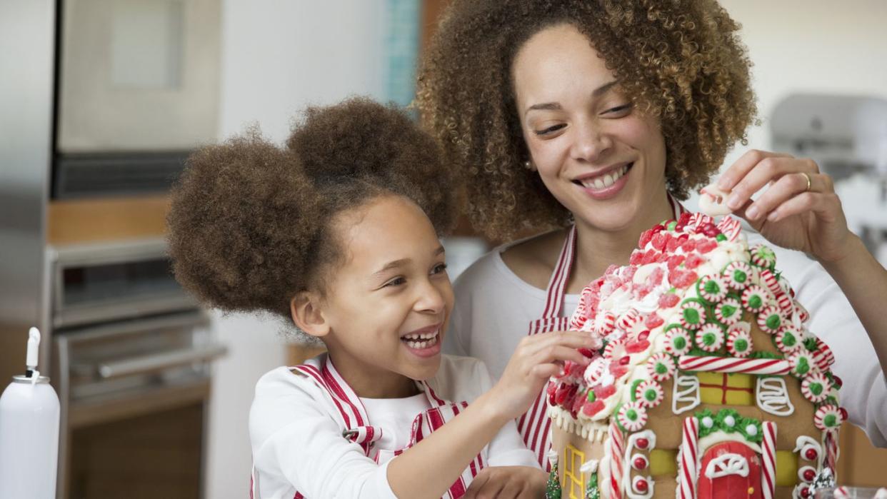 black mother and daughter decorating gingerbread house