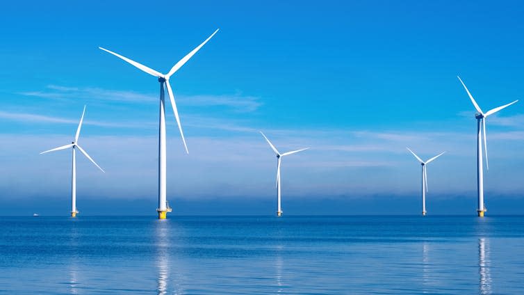 Six large white wind farms offshore, calm waters, clear blue sky