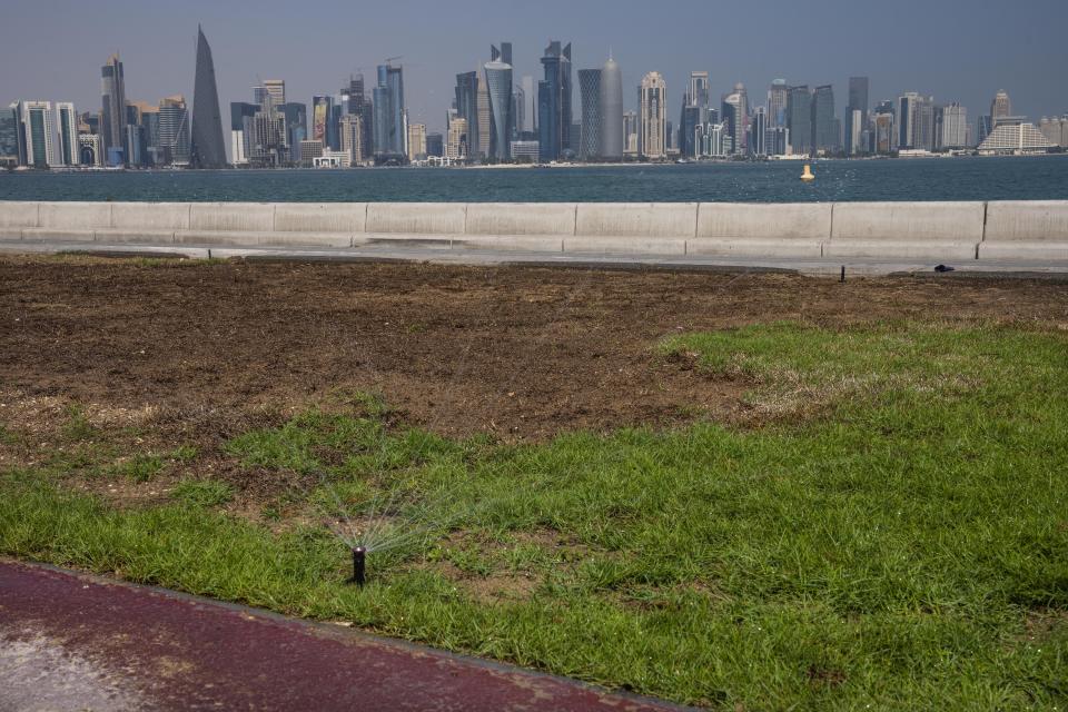 FILE - A water sprinkler on the corniche, overlooking the skyline of Doha, Qatar, Wednesday, Oct. 19, 2022. Qatar unveiled a plan last October to cut its emissions by a quarter by 2030. Then, Russia invaded Ukraine and made the Persian Gulf nation's liquid natural gas only more sought after. Demand for fossil fuels has brought immense wealth to Qatar, but in the coming decades, it could also make one of the world's hottest places unlivable. (AP Photo/Nariman El-Mofty, File)