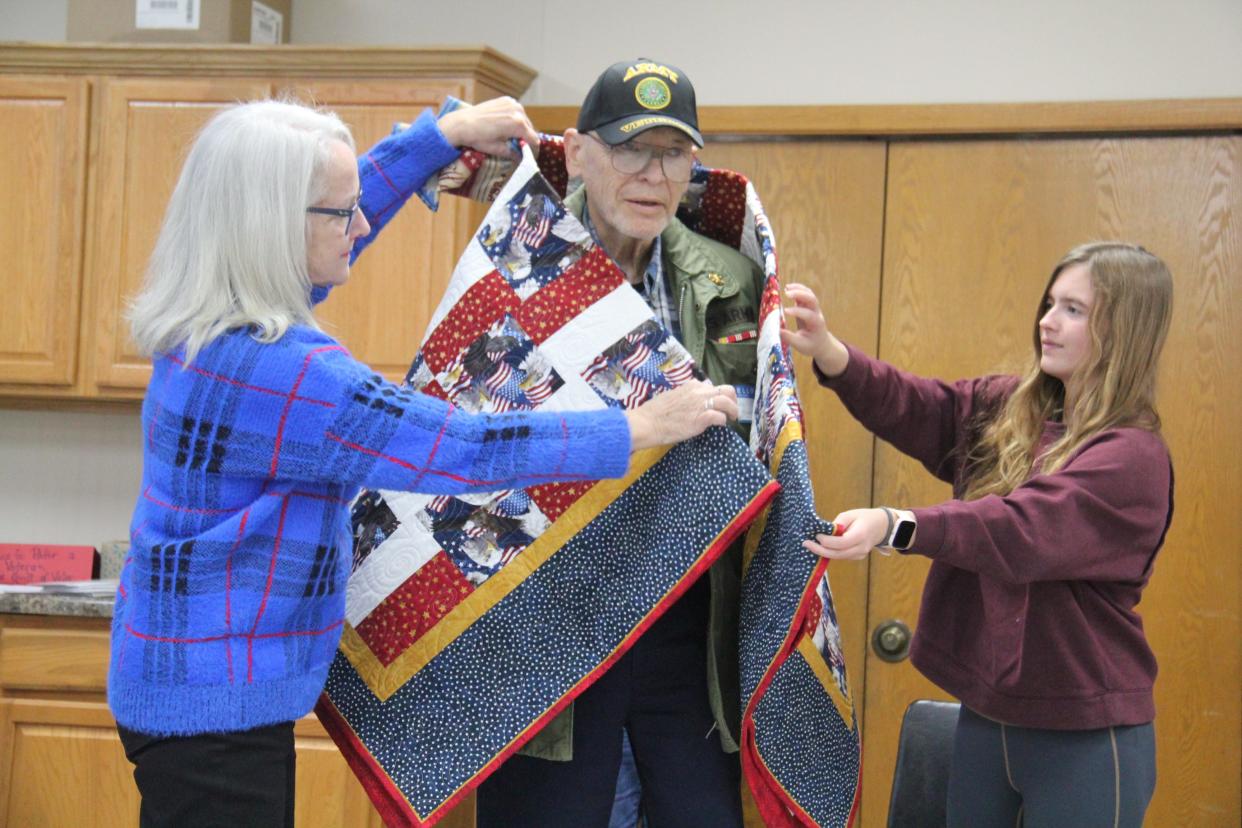 Perry Piecemakers and family members help wrap Lou Hoger in a Quilt of Valor during a presentation on on Friday, Nov. 10, 2023, at the Perry Elks Lodge.