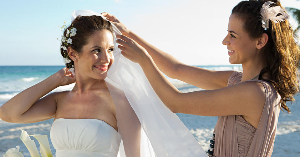 Picture of a bride getting her veil adjusted by her bridesmaid who is in a tan dress.