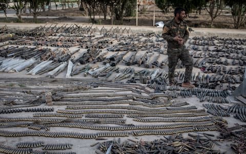 An SDF fighter looks over seized Isil weapons that were found in the last stronghold of the extremist group as they were displayed at an SDF base - Credit: Getty