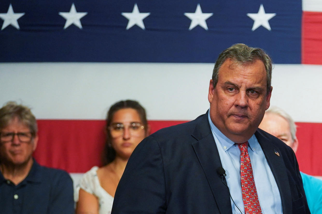 Former New Jersey Governor Chris Christie stands in front of a large American flag, with a few supporters behind him, as he launches his White House bid.