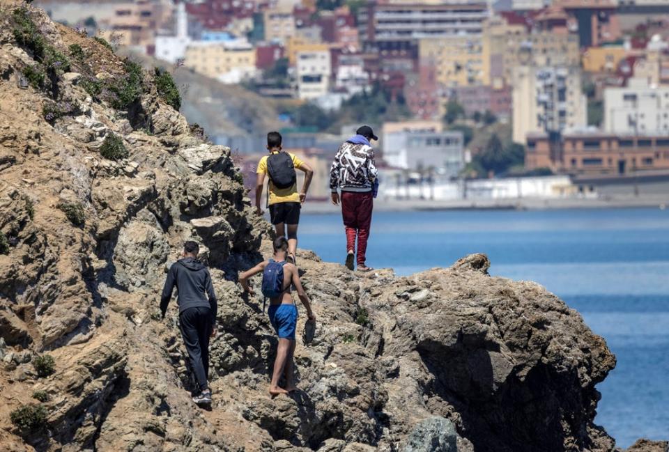 Moroccan migrants climb a cliff as they attempt to cross the border to Spain’s north African enclave of Ceuta, 19 May 2021 (AFP/Getty)