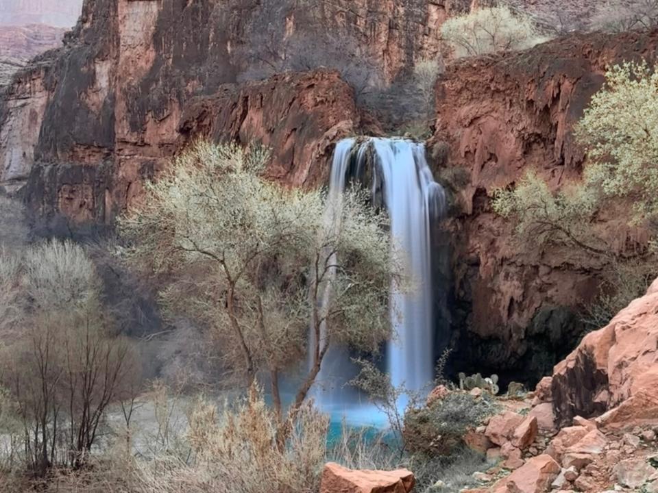 A blue waterfall cascading down red rocks surrounded by trees.