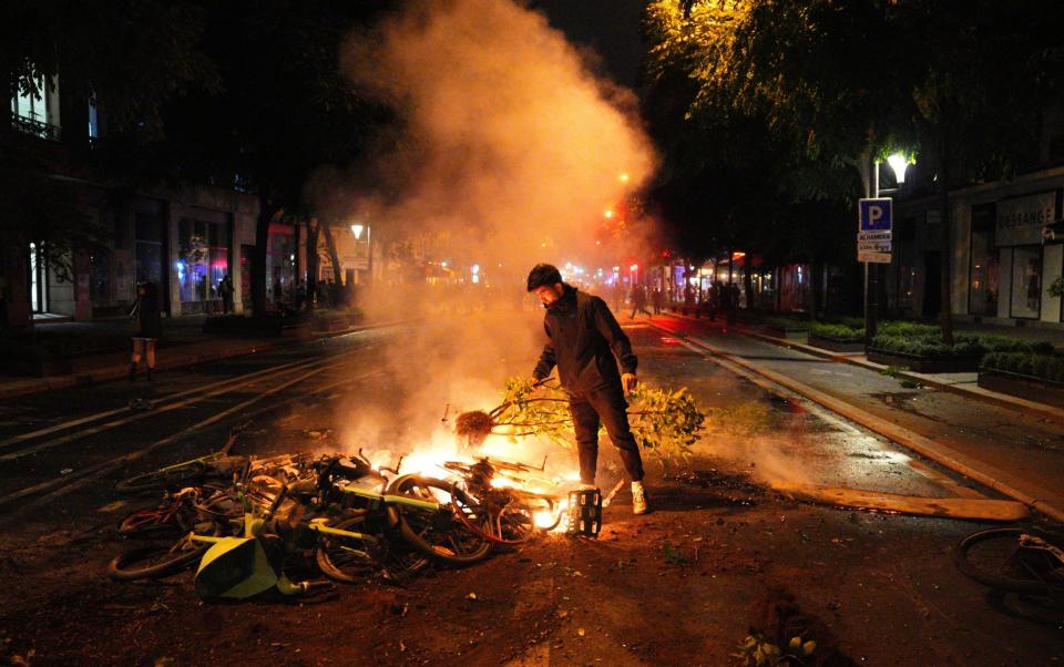 A man places an uprooted plant on a pile of burning e-bikes during a protest