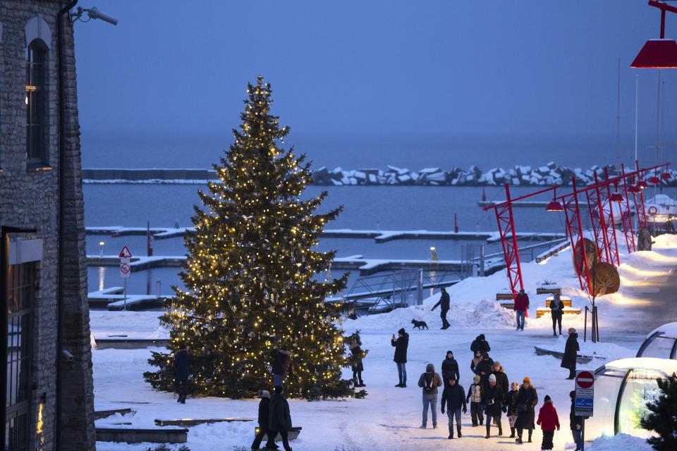 People walk around a Christmas tree decorated for the Christmas and New Year festivities at the Noblessner port in the Tallinn Bay, Estonia, Saturday, Dec. 16, 2023. In Estonia, as in many parts of the world, trees covered with lights brighten up homes and town squares during the Winter Solstice and Christmas festivities afterwards. (AP Photo/Pavel Golovkin)