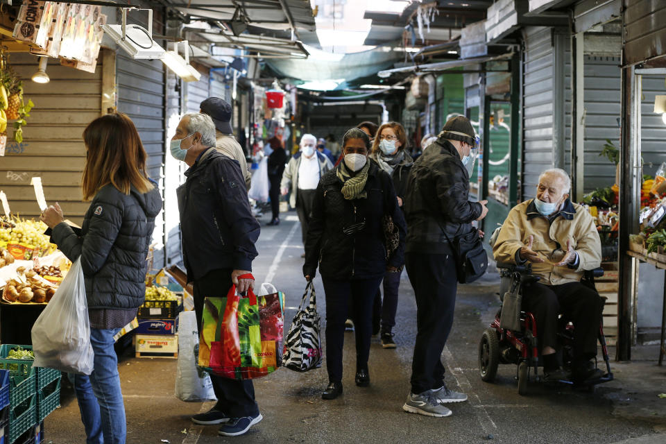 People wearing masks hold bags while shopping at an open-air market in Rome, Thursday, Oct. 22, 2020. Authorities in regions including Italy's three largest cities have imposed curfews in a bid to slow the spread of COVID-19 where it first struck hard in Europe, most of whose countries are now imposing, or mulling, new restrictions to cope with rapidly rising caseloads. (Cecilia Fabiano/LaPresse via AP)