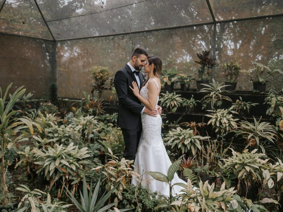 A bride and groom embrace in a green house.