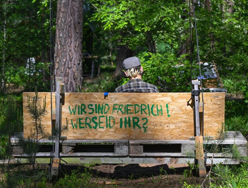 An activist from the "Stop Tesla" initiative sits in a forest near the Tesla Gigafactory Berlin-Brandenburg plant on a bench with the inscription "We are Friedrich! Who are you?". According to the police, more than 1,000 activists marched from Fangschleuse station to the Tesla factory. Patrick Pleul/dpa