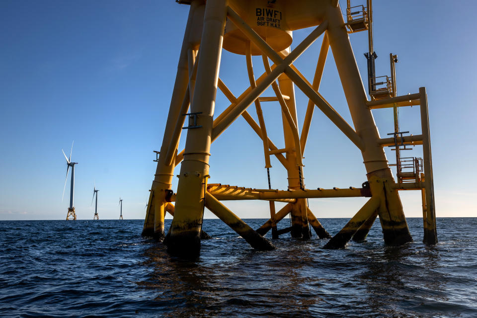Several large wind turbines rest on yellow platforms in the ocean.