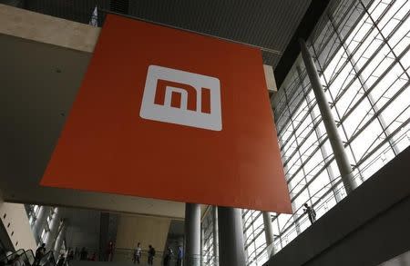 People stand near a logo of Xiaomi ahead of the launching ceremony of Xiaomi Phone 4, in Beijing, July 22, 2014. REUTERS/Jason Lee