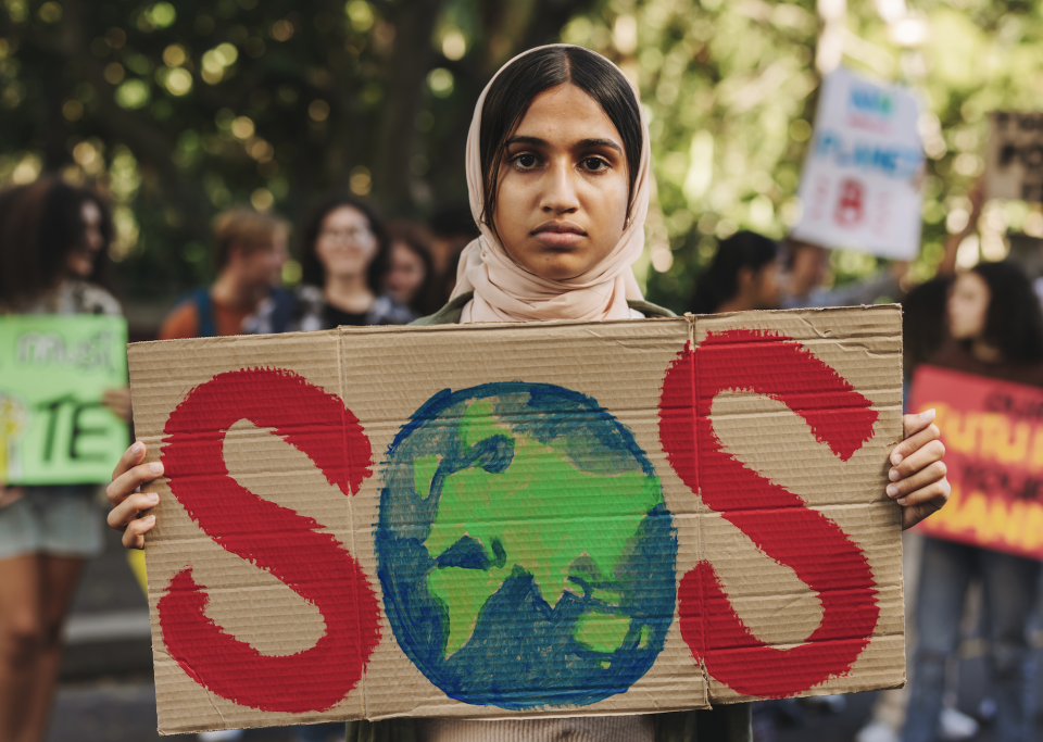 Young woman wearing a hijab while holding a protest sign that reads "SOS"