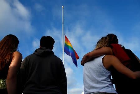 Mourners gather under a LGBT pride flag flying at half-mast for a candlelight vigil in remembrance for mass shooting victims in Orlando, from San Diego, California, U.S. June 12, 2016. REUTERS/Mike Blake