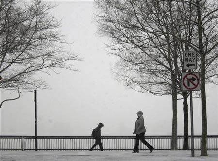 People walk in a park along the Hudson River across from New York as snow begins to fall in Hoboken, New Jersey January 21, 2014. REUTERS/Gary Hershorn