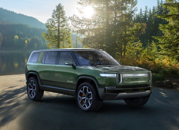 The Rivian R1S, a boxy green SUV with a futuristic front end, in a wooded setting.