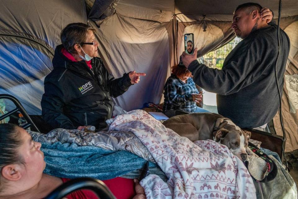 Holly Porter, who is functionally quadriplegic, watches from the hospital bed in her tent as Tracey Knickerbocker with Hope Cooperative talks to Justin Smith of Sacramento County Department of Human Assistance on a mobile phone held by care navigator Nate Guerra in February. They were giving Porter a video tour of a possible apartment which she decided not to take.
