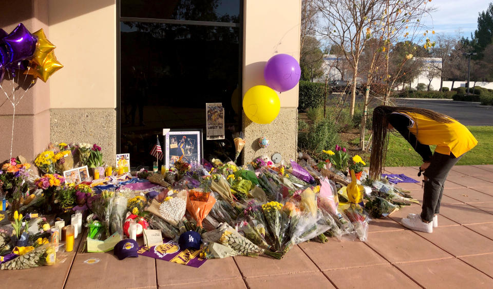 Wearing a Kobe Bryant No. 8 Lakers jersey, Olivia Tyler, 19, of Simi Valley, Calif., views the memorial at the Mamba Sports Academy in Thousand Oaks, Calif., and pray for the families of the victims of the Sunday helicopter crash that took the lives of the former Lakers star and eight others, Monday morning, Jan. 27, 2020. Tyler said she has idolized Bryant for years and that she previously played at the sports academy but before Bryant bought it. She met him at a UCLA basketball game in 2017 and he gave her a high-five. "Kobe taught me a lot about being the first person in the gym and the last one out," she said. (AP Photo/Stefanie Dazio)