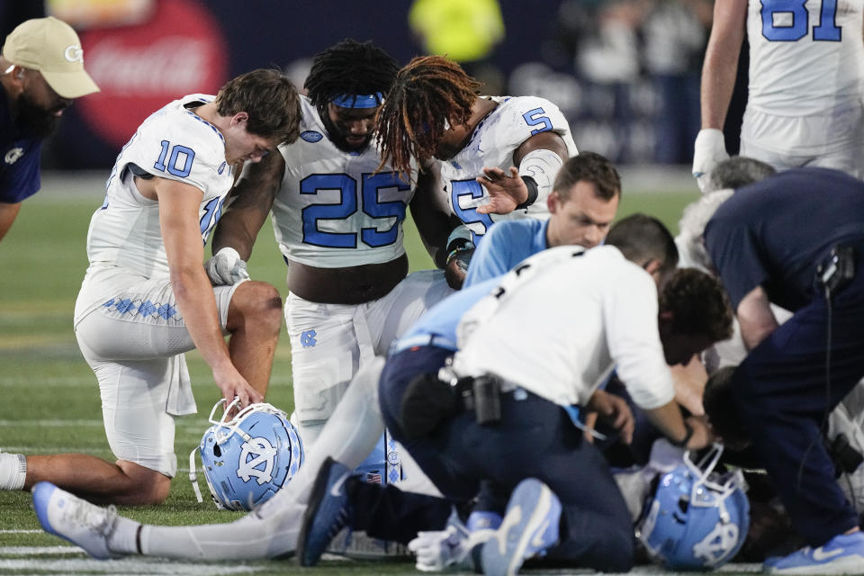 North Carolina players Drake Maye (10) Kaimon Rucker (25) and J.J. Jones (5) pray as North Carolina wide receiver Devontez Walker (9) is attended to after being injured during the second half of an NCAA college football game against Georgia Tech , Saturday, Oct. 28, 2023, in Atlanta. (AP Photo/John Bzemore)