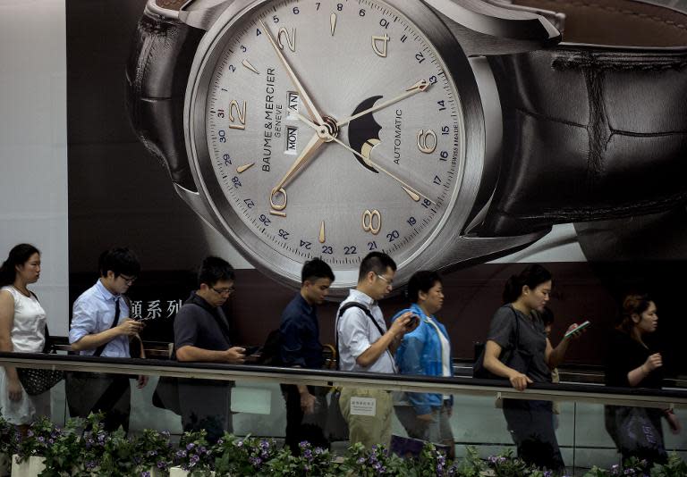 People are seen on a moving walkway next to a large advertisement for a luxury watch, in Hong Kong, on August 7, 2014