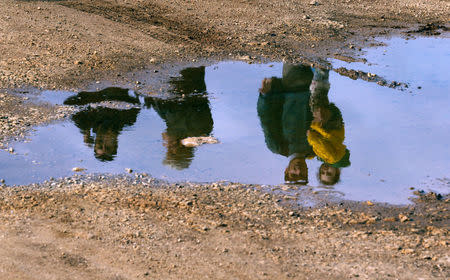 Syrian refugees are reflected in a puddle as they wait on a roadside after Turkish police prevented them from sailing off to the Greek island of Farmakonisi by dinghies, near a beach in the western Turkish coastal town of Didim, Turkey March 9, 2016. REUTERS/Umit Bektas