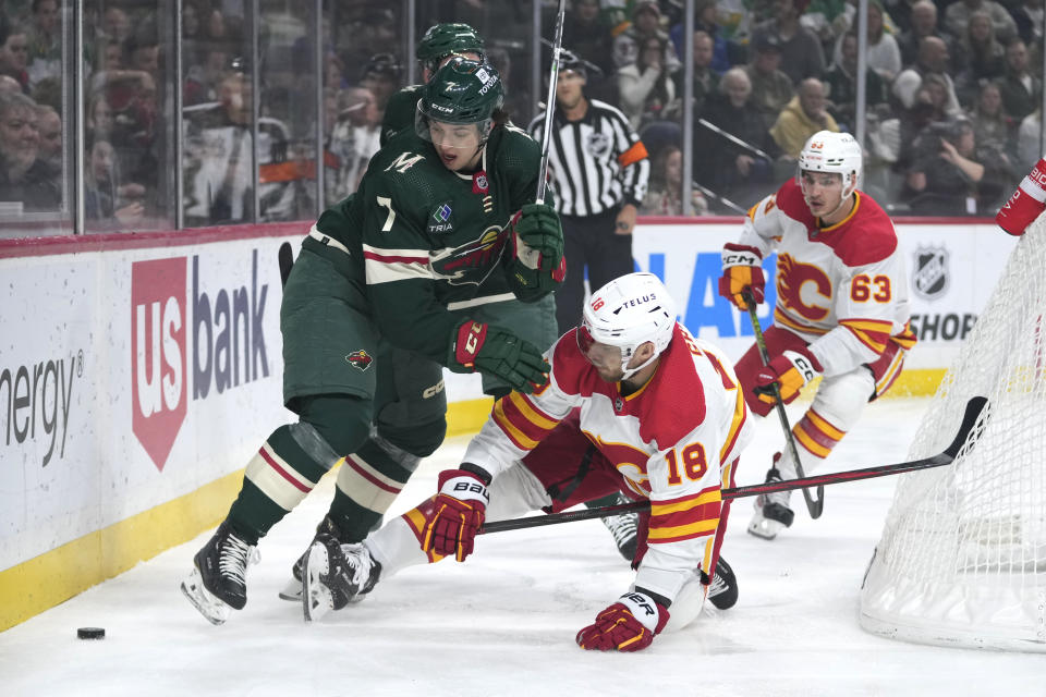 Minnesota Wild defenseman Brock Faber (7) and Calgary Flames left wing A.J. Greer (18) vie for the puck during the first period of an NHL hockey game Tuesday, Jan. 2, 2024, in St. Paul, Minn. (AP Photo/Abbie Parr)
