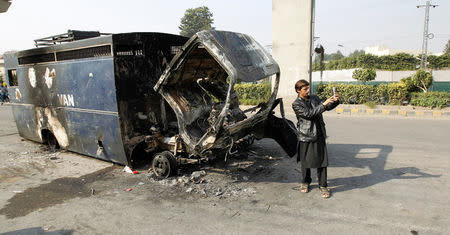 A passerby takes a selfie in front of a police prison van destroyed during clashes with police near the Faizabad junction in Islamabad, Pakistan November 26, 2017. REUTERS/Caren Firouz