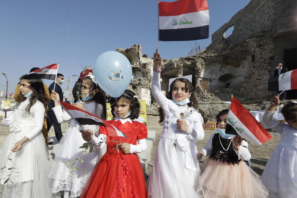 Children in their festive garment wave Iraqi flags to the camera as they arrive to join Pope Francis who will pray for the victims of war at Hosh al-Bieaa Church Square, in Mosul, Iraq, once the de-facto capital of IS, Sunday, March 7, 2021. The long 2014-2017 war to drive IS out left ransacked homes and charred or pulverized buildings around the north of Iraq, all sites Francis visited on Sunday. (AP Photo/Andrew Medichini)