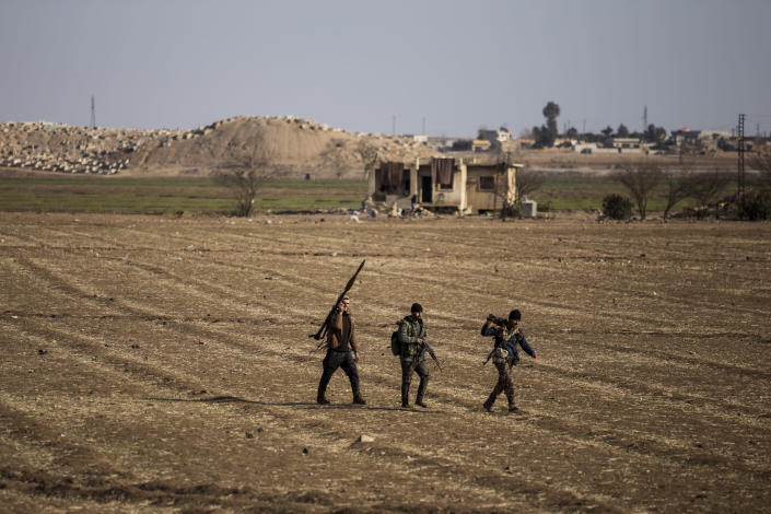 Syrian Democratic Forces fighters walk in a field in Hassakeh, northeast Syria, Wednesday, Jan. 26, 2022. Dozens of armed Islamic State militants remained holed up in the last occupied section of a Syrian prison, U.S.-backed Kurdish-led forces said Thursday. The two sides clashed a day after the Syrian Democratic Forces announced they had regained full control of the facility. (AP Photo/Baderkhan Ahmad)