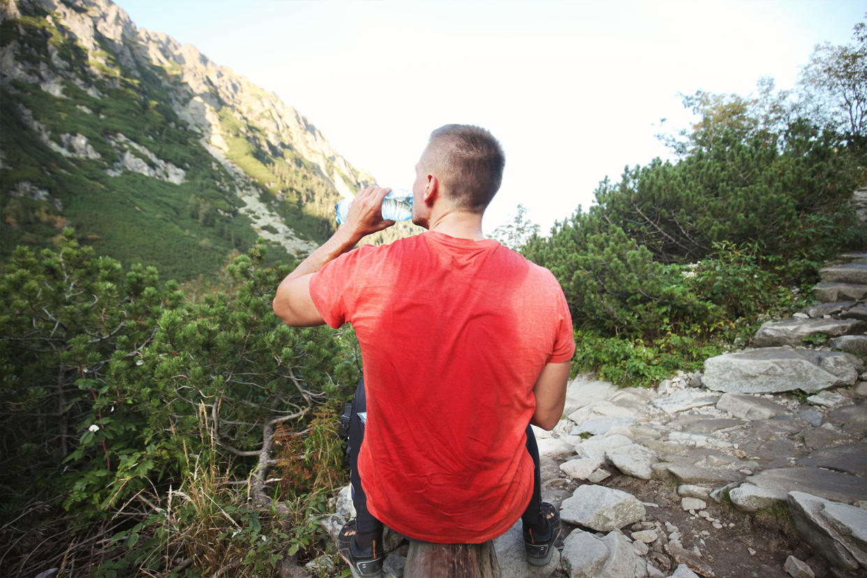 Man after trekking with sweaty t-shirt drinking water against mountains Getty Images/Stanislaw Pytel