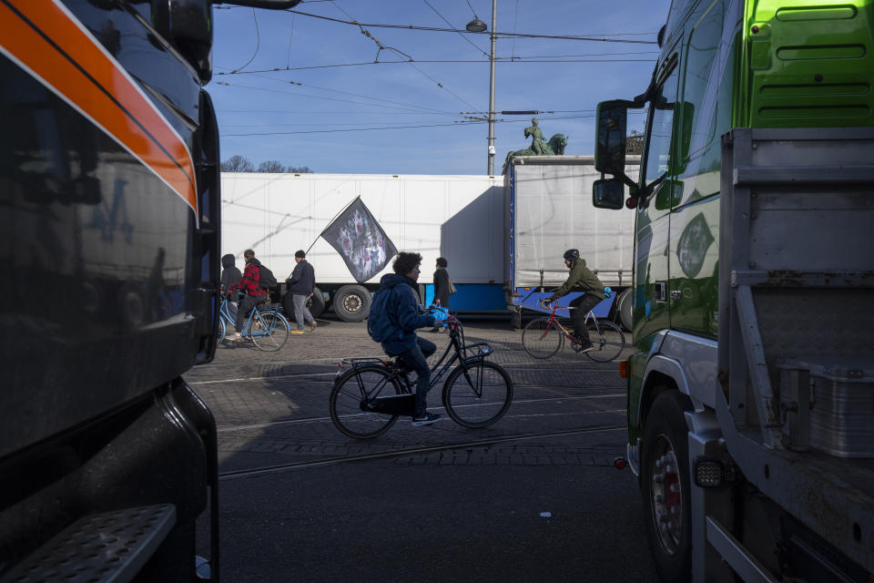 Bicyclists pass some of the 20 trucks blocking one entrance to the government buildings in The Hague, Netherlands, Saturday, Feb. 12, 2022, to protest against COVID-19 restrictions. The events are in part inspired by protesters in Canada. (AP Photo/Peter Dejong)