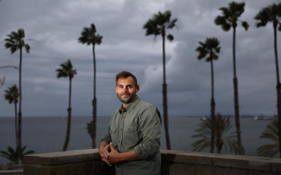 Paul Piff poses in front of palm trees and the ocean in Long Beach.