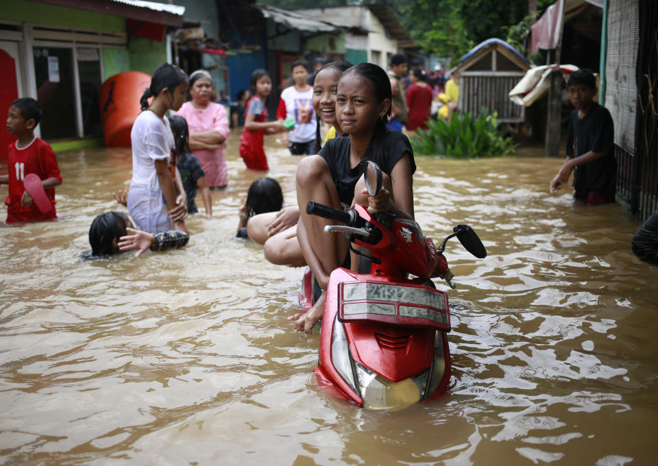Indonesian girls sit on a motorcycle at a flooded neighborhood in Jakarta, Indonesia, Tuesday, Feb. 21, 2017. Torrential rains in the Indonesian capital have overwhelmed drains and flooded roads and thousands of homes. Floods and deadly landslides are a fact of life for Indonesians during the wet season, with other major cities suffering repeated flooding. (AP Photo/Dita Alangkara)