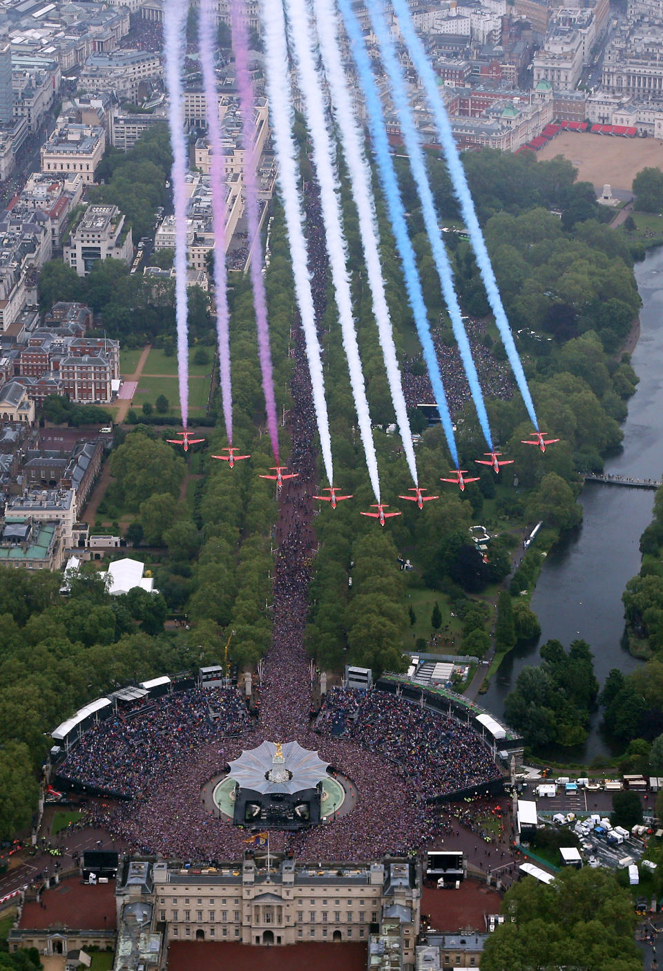 Red, white and blue streaming out from behind them the Royal Air Force Aerobatic Team fly in formation over Buckingham Palace as the Royal Family stand on the balcony.