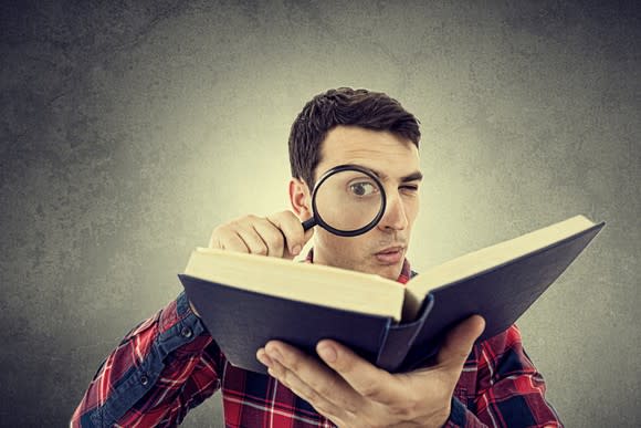 Man reading a book with a magnifying glass.