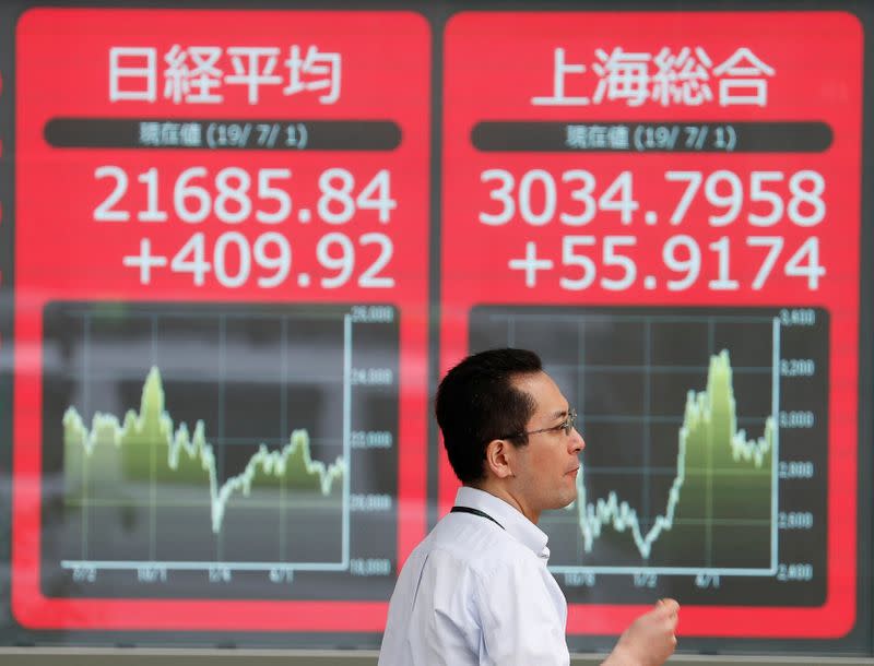 A man walks past an electric screen showing Japan's Nikkei and Shanghai Stock Exchange markets' indices outside a brokerage in Tokyo