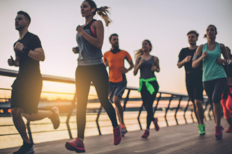 Group of young people competing in a race. Young men and women running on riverside promenade at sunset. They are wearing sport clothing.