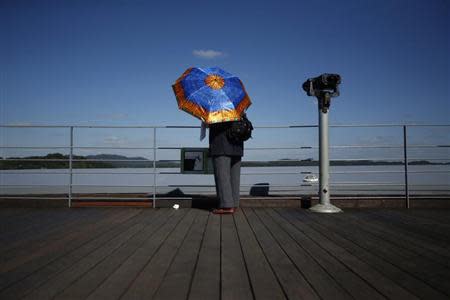 A woman holding an umbrella stands next to a pair of binoculars for tourists at the Imjingak pavilion near the demilitarized zone which separates the two Koreas, in Paju, north of Seoul October 16, 2013. REUTERS/Kim Hong-Ji