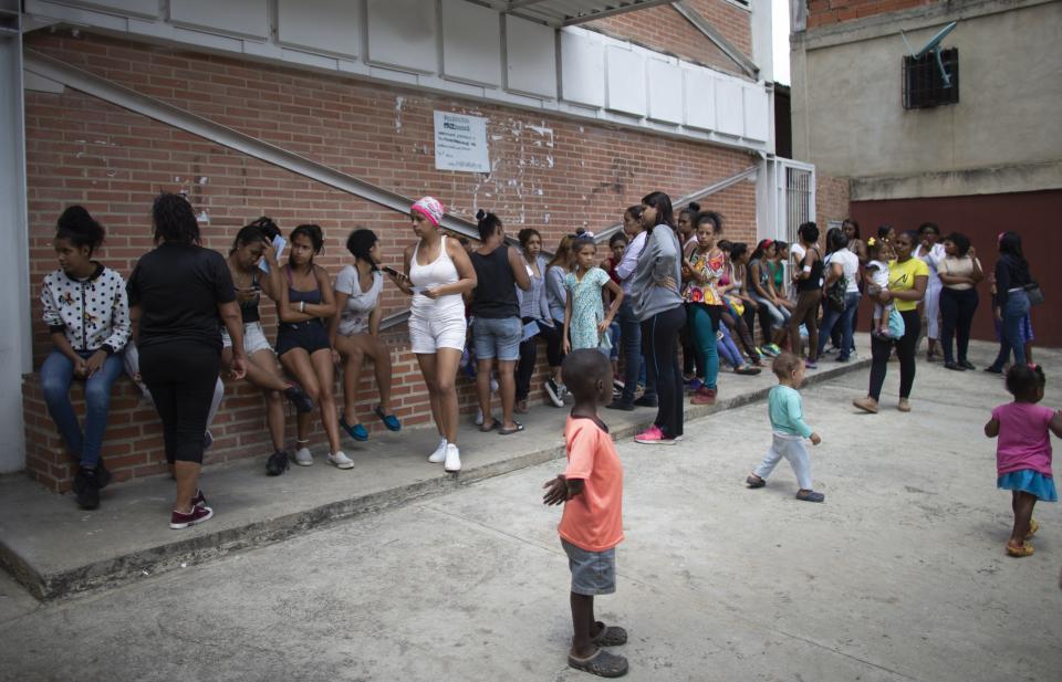 In this photo taken July 25, 2019, women with their children wait outside a clinic in hopes of getting information on the next time hormonal implants to prevent pregnancies will be available, after the clinic ran out in the Caucaguita neighborhood on the outskirts of Caracas, Venezuela. The 104 implants available were not enough for the women who wanted one. (AP Photo/Ariana Cubillos)