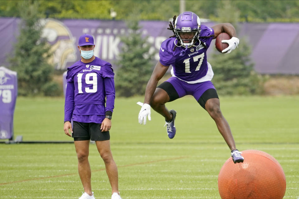 Minnesota Vikings wide receiver K.J. Osborn (17) runs a pass play, leaping over a large ball, as wide receiver Adam Thielen watches during the NFL football team's training camp, Thursday, Aug. 5, 2021, in Eagan, Minn. (AP Photo/Jim Mone)