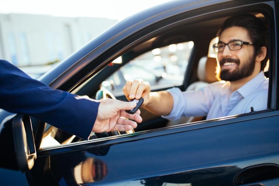 Smiling man sitting in a car being handed they key