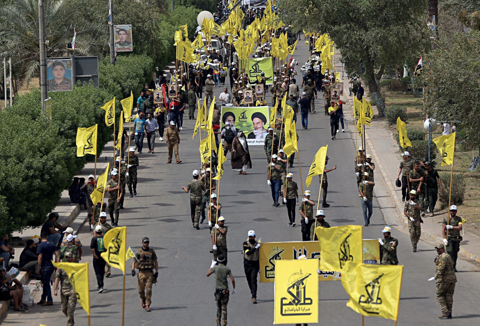 FILE - In this June 8, 2018 file photo, Iraqi Popular Mobilization Forces march as they hold their flag and posters of Iraqi and Iranian Shiites spiritual leaders during "al-Quds" or Jerusalem Day, in Baghdad, Iraq. Iran-aligned Shiite militias are posing an increasing challenge for Iraq ahead of key talks with Washington in early April 2021, that are meant to shape the future of the U.S.-Iraq relationship. (AP Photo/Hadi Mizban, File)